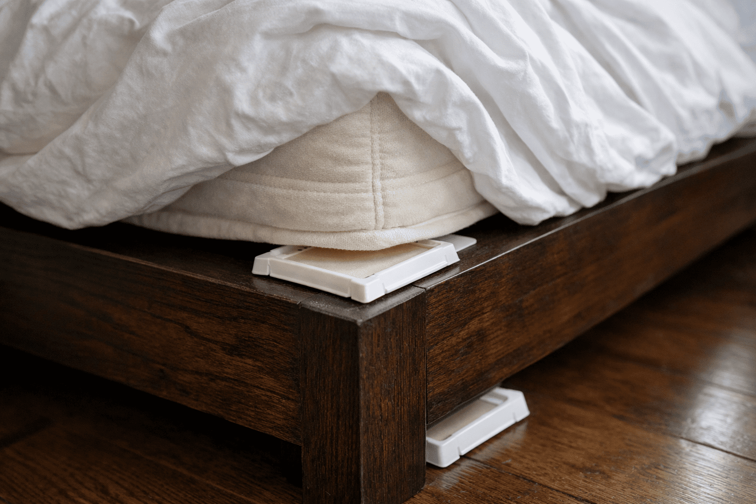 Bed bug monitor trap positioned under mattress corner in bedroom for pest detection and monitoring