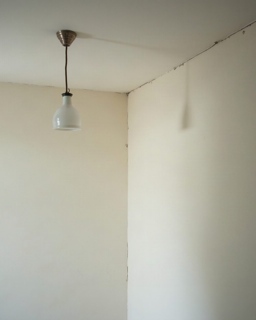 Plain white ceiling meeting a wall in a lit room, a pendant light fitting at one edge, shallow angle looking upward
