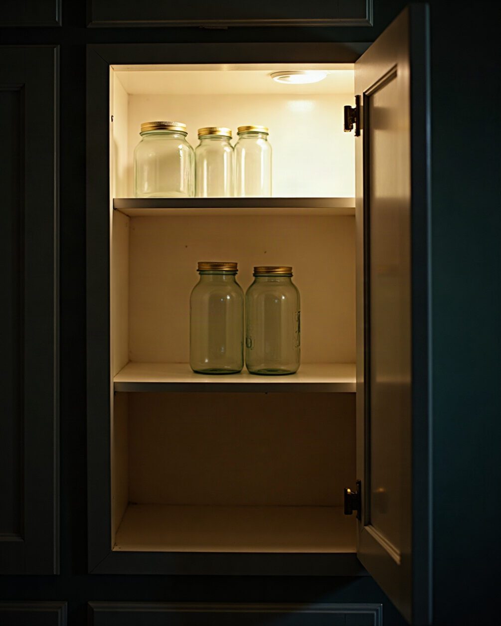 Open kitchen cupboard seen from below with plain glass jars on the top shelf and the underside of the shelf above
