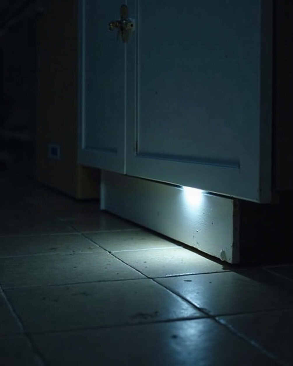 Kitchen floor at night with the light just on, the gap beneath a kickboard and a skirting board visible