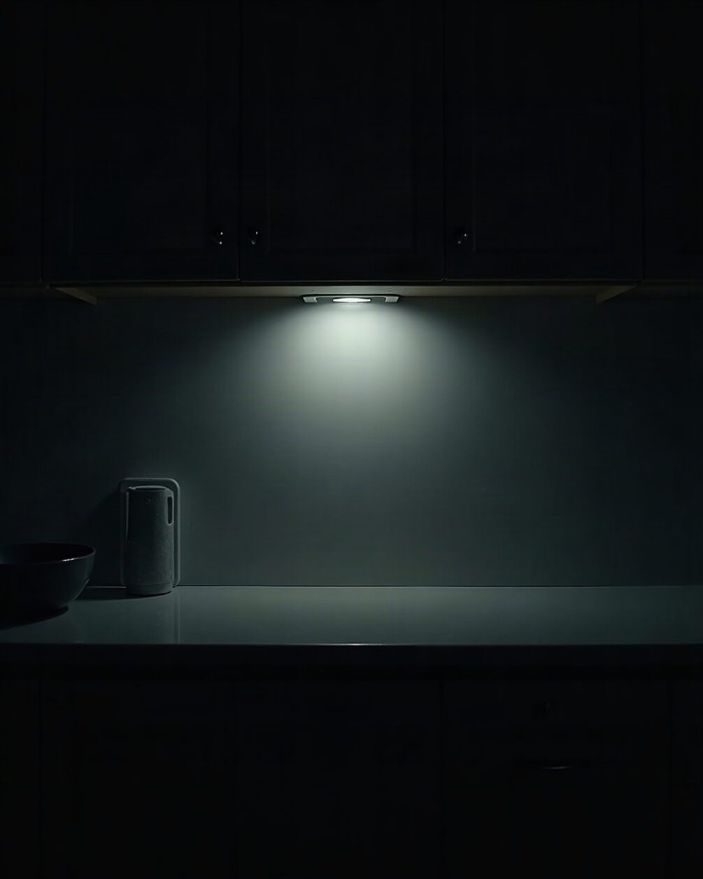 Dark kitchen at night with a single light just switched on over an empty worktop